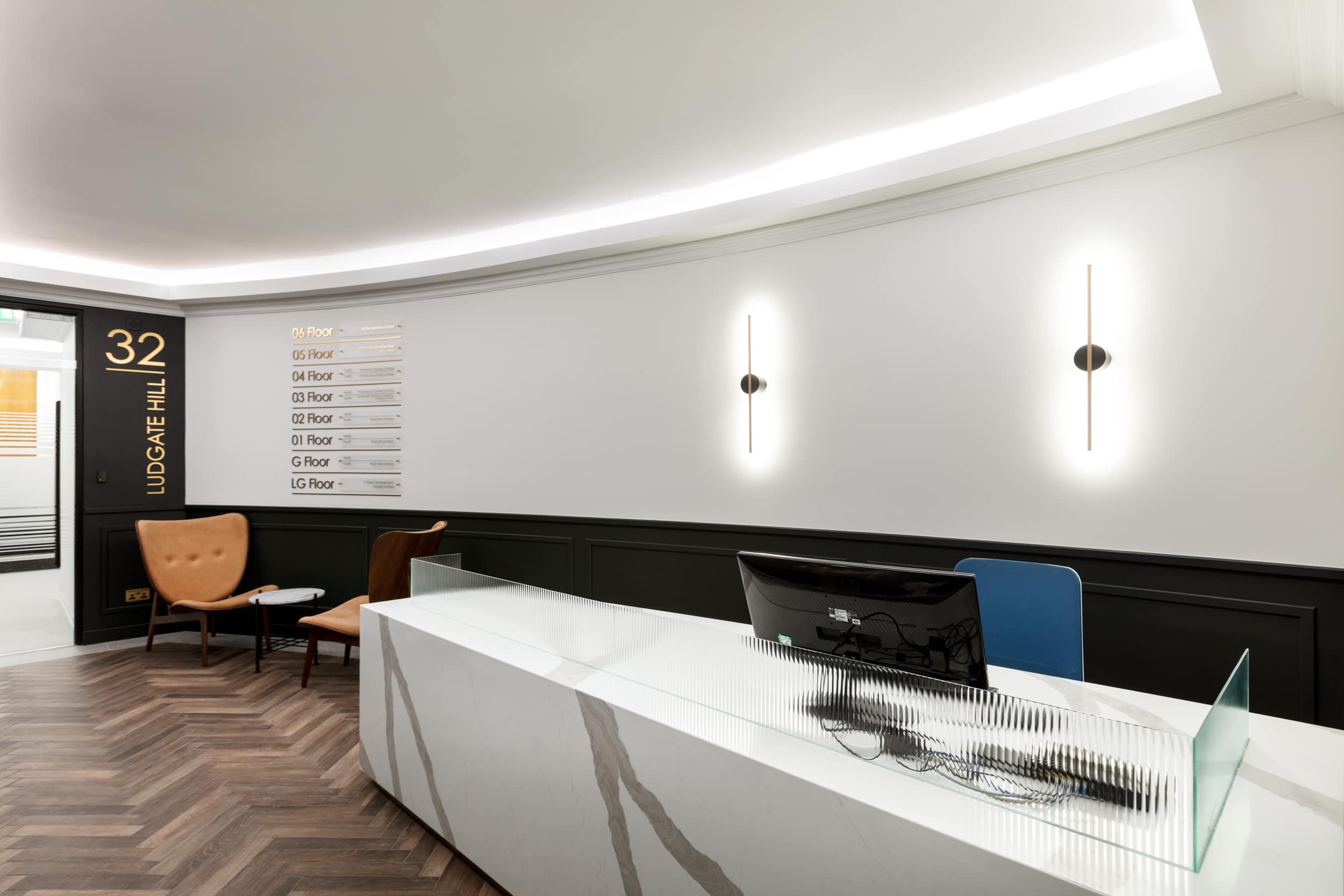 Reception area at 32 Ludgate Hill featuring a modern desk, two brown chairs, and a wall-mounted directory of floors.