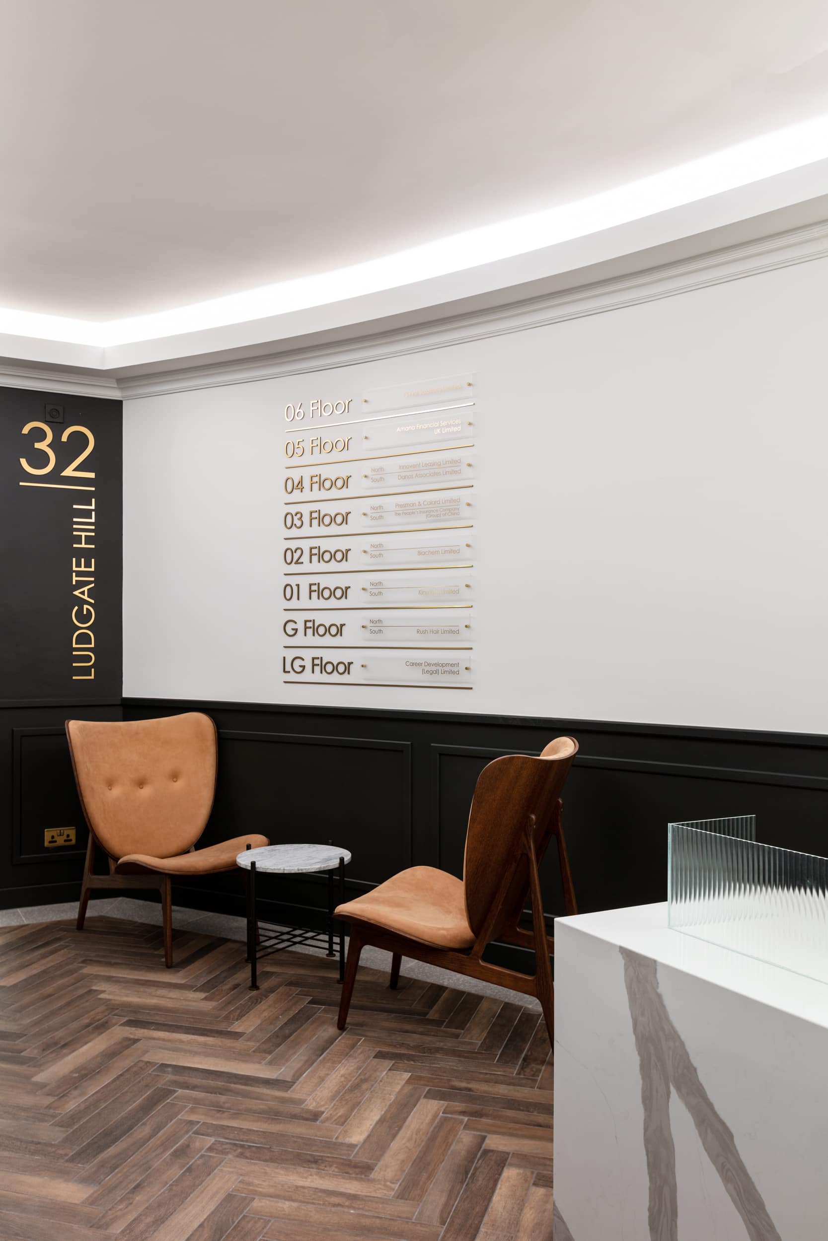 Interior view of a waiting area at 32 Ludgate Hill, featuring two chairs, a small table, and a wall-mounted directory listing the floors and tenants.