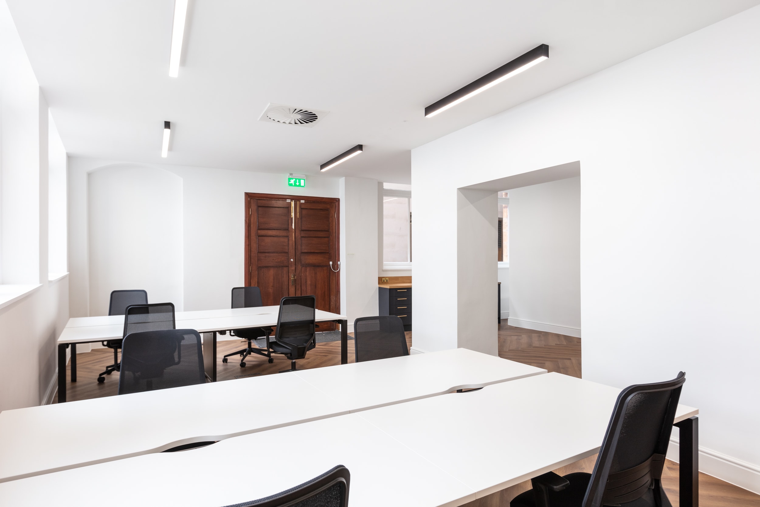Modern office space featuring white desks and black mesh chairs, with wooden doors and natural light from windows.