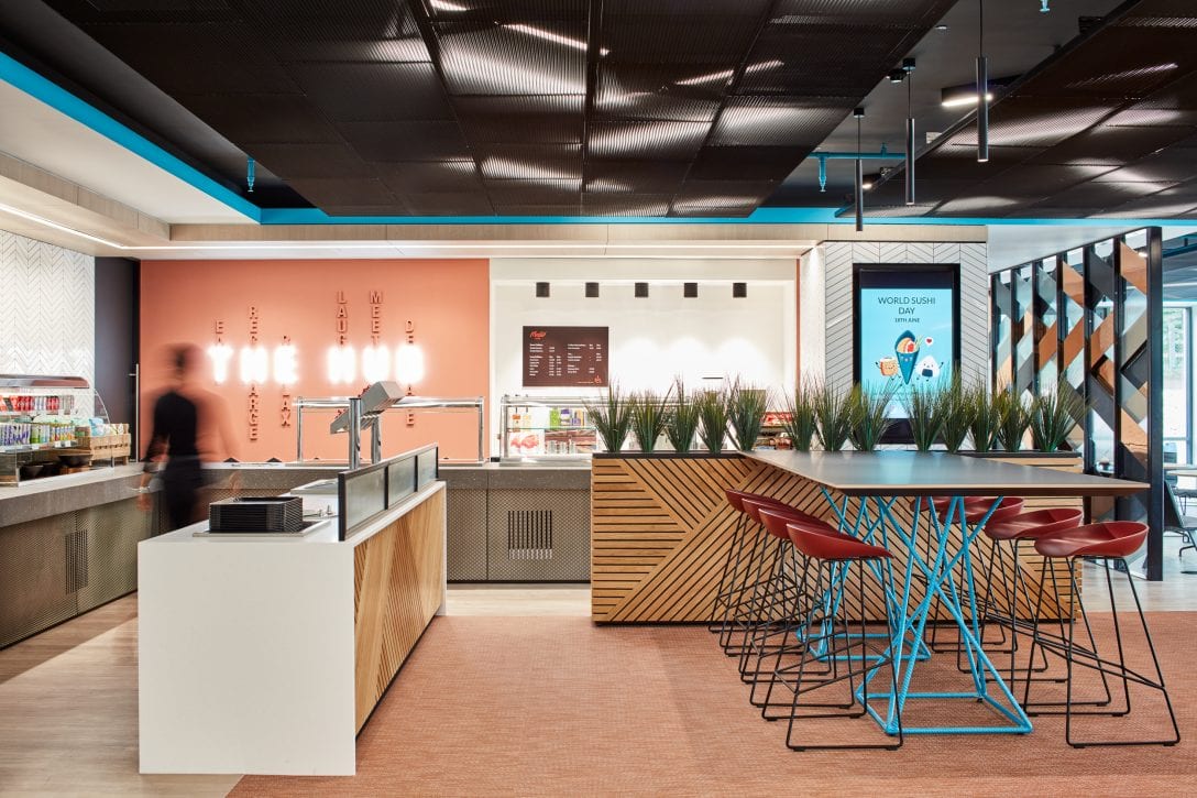 A woman is shown walking through an office canteen which promotes a healthy menu to promote workplace wellness. 