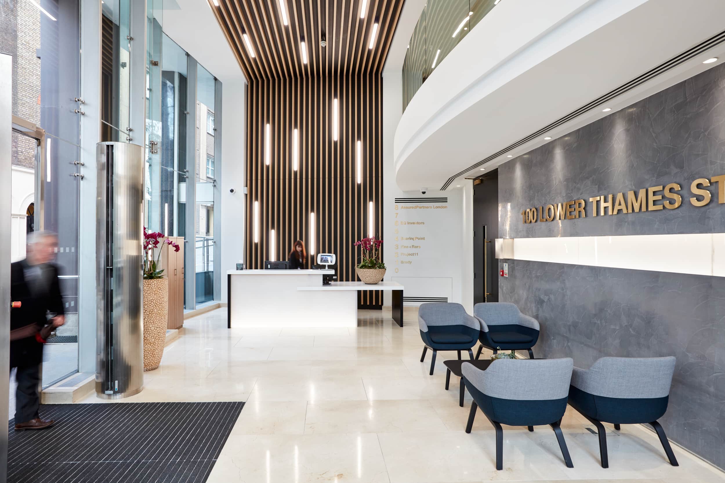 Modern reception area at 100 Lower Thames, featuring a front desk, seating, and decorative elements, with large windows allowing natural light.