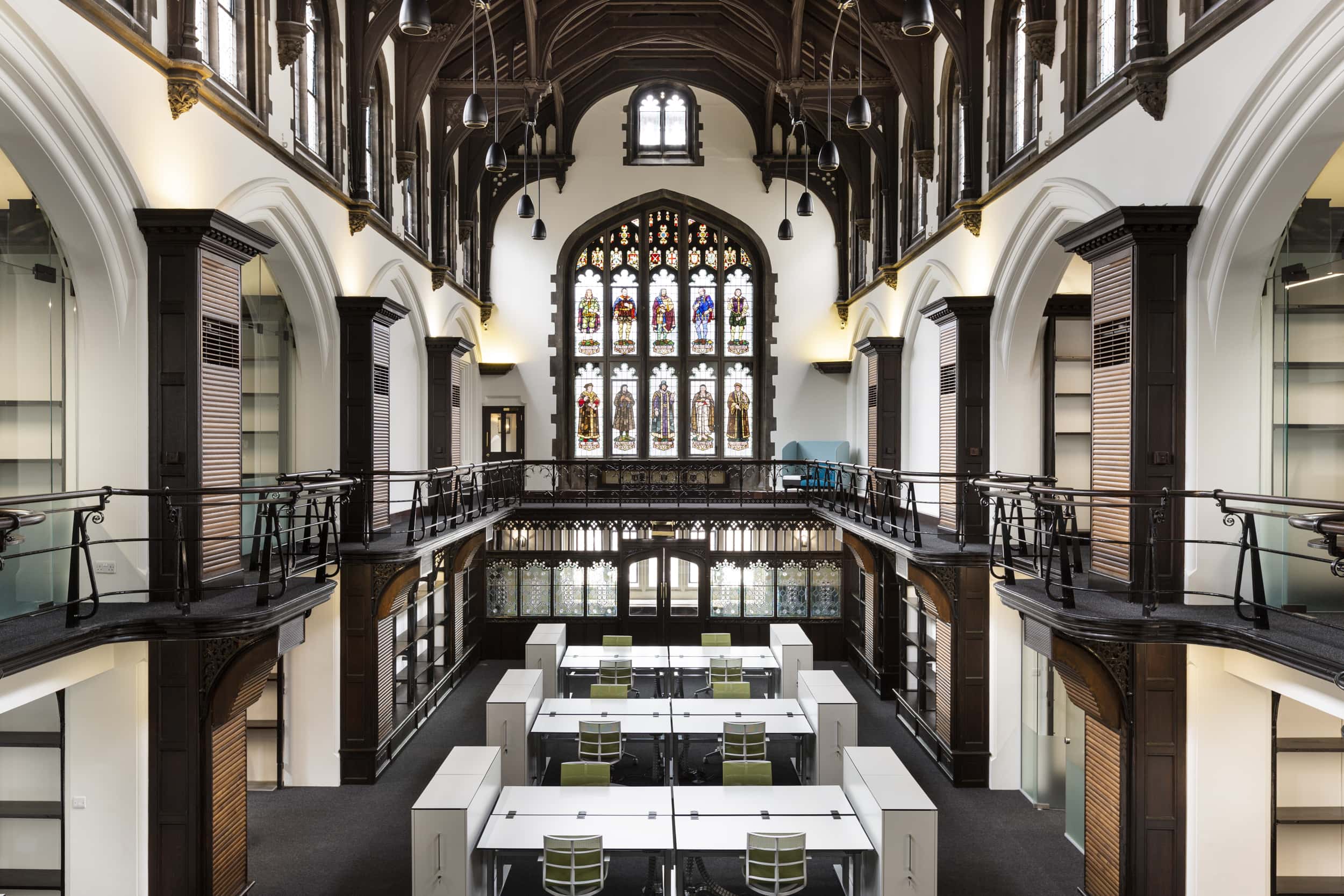 Interior view of Allianz Sion Hall featuring a high ceiling with wooden beams, large stained glass windows, and modern workstations arranged below.