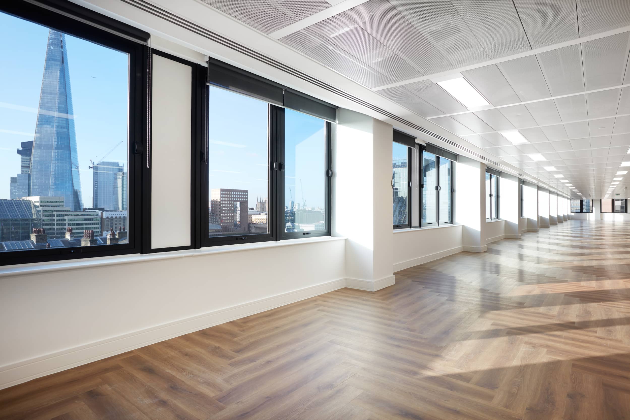 Bright, modern office space with large windows showcasing a city skyline, featuring the Shard in the background and wooden flooring.