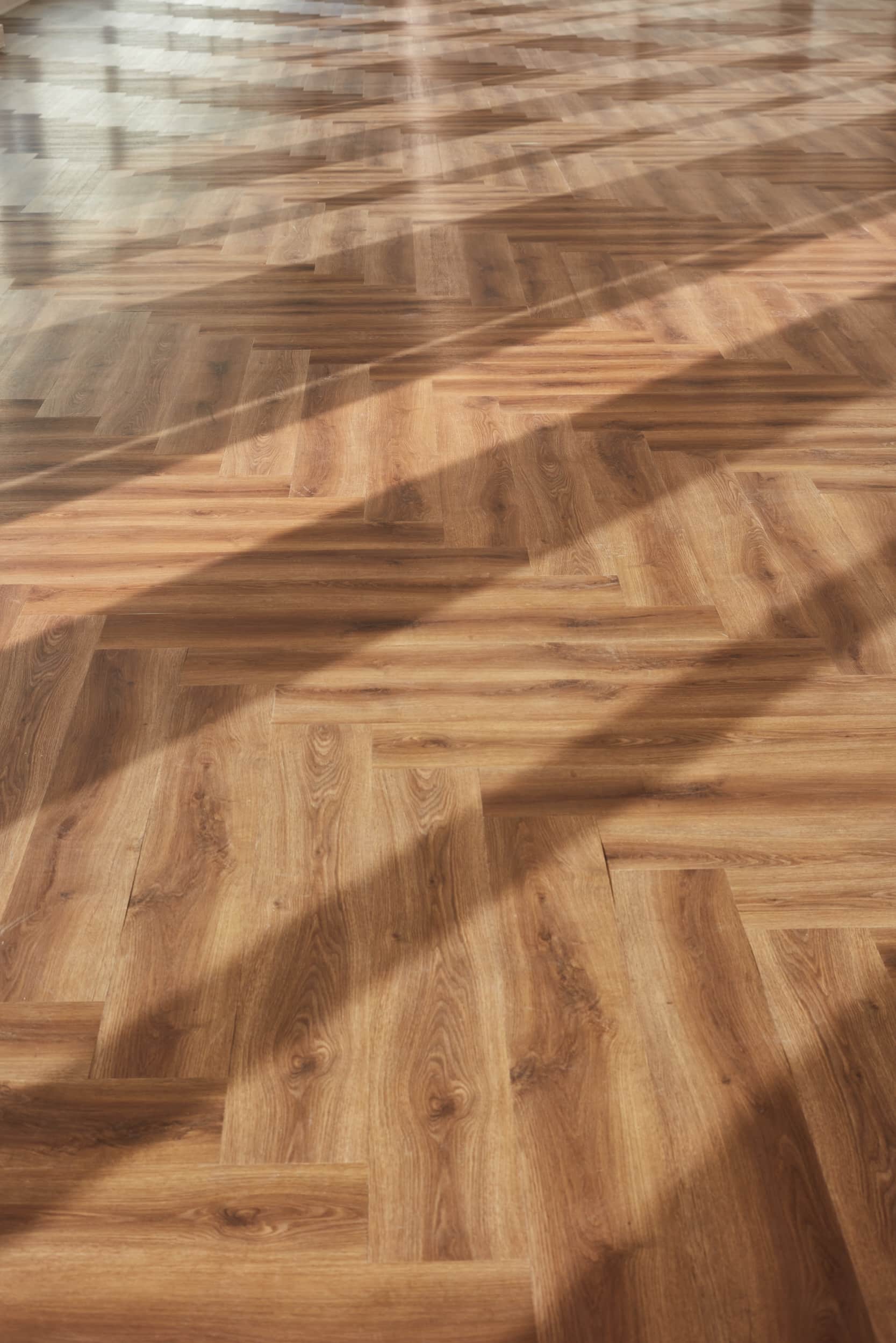 Wooden herringbone-patterned flooring with shadows cast across the surface.
