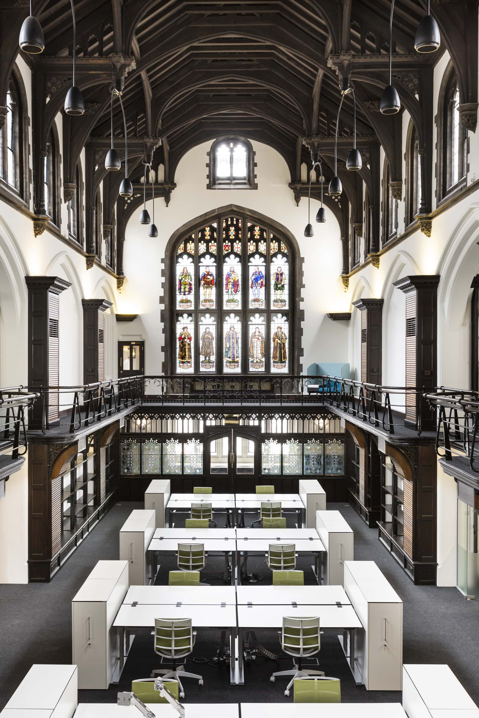Interior view of Allianz Sion Hall featuring a high wooden ceiling, large stained glass windows, and modern workstations with green chairs.