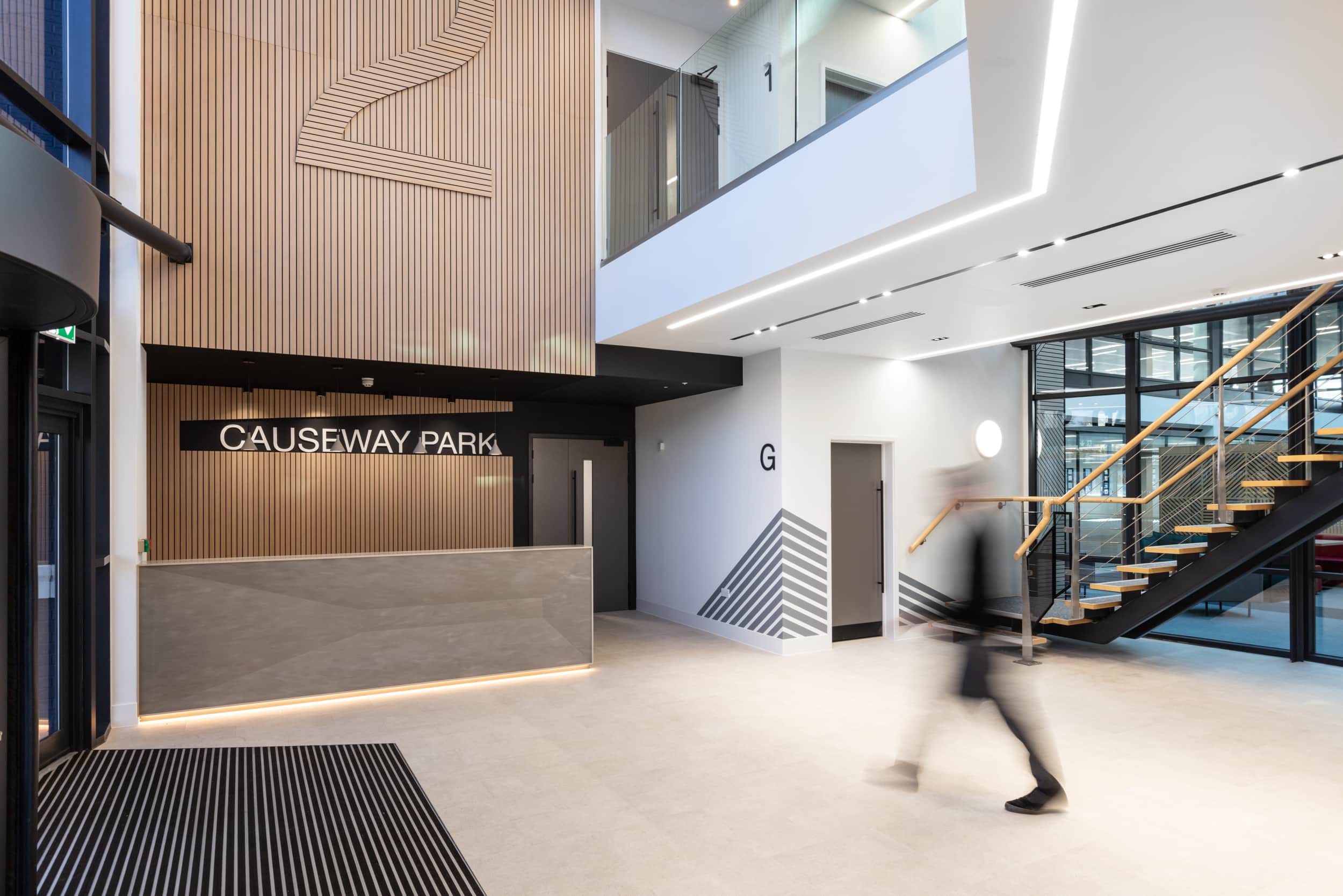 Interior view of Causeway Park featuring a reception area with wooden paneling, a gray counter, and a staircase in the background.