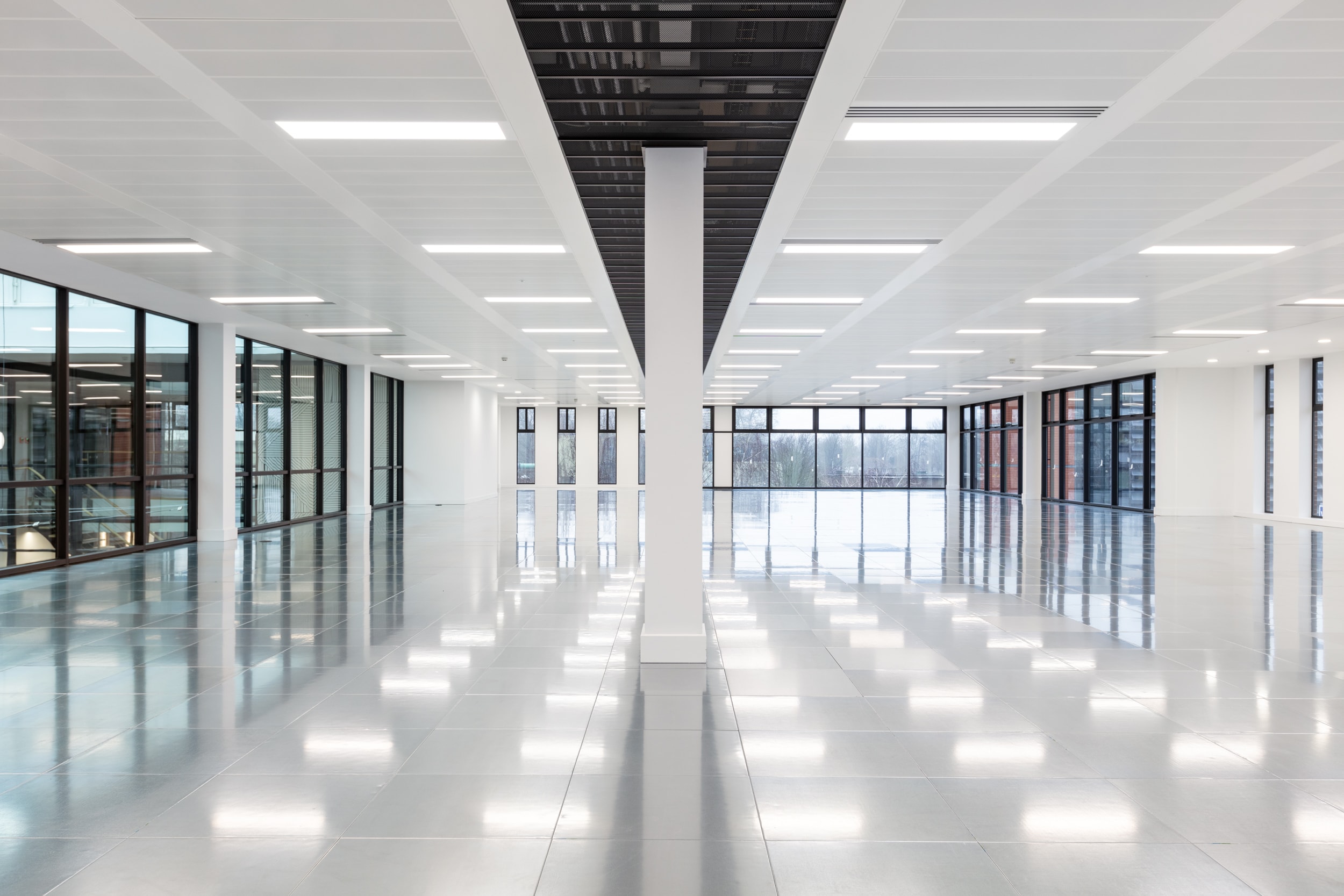 Spacious, modern interior of an office space with polished floors, large windows, and bright overhead lighting.