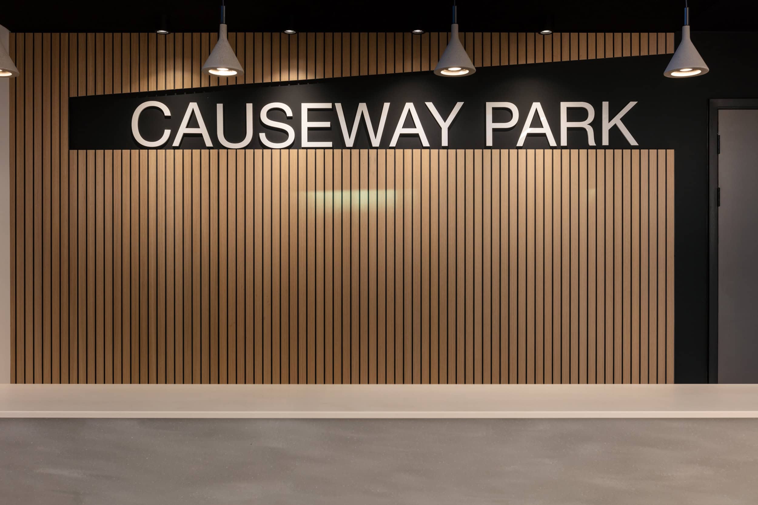Signage displaying "CAUSEWAY PARK" on a wooden slatted wall with pendant lighting.