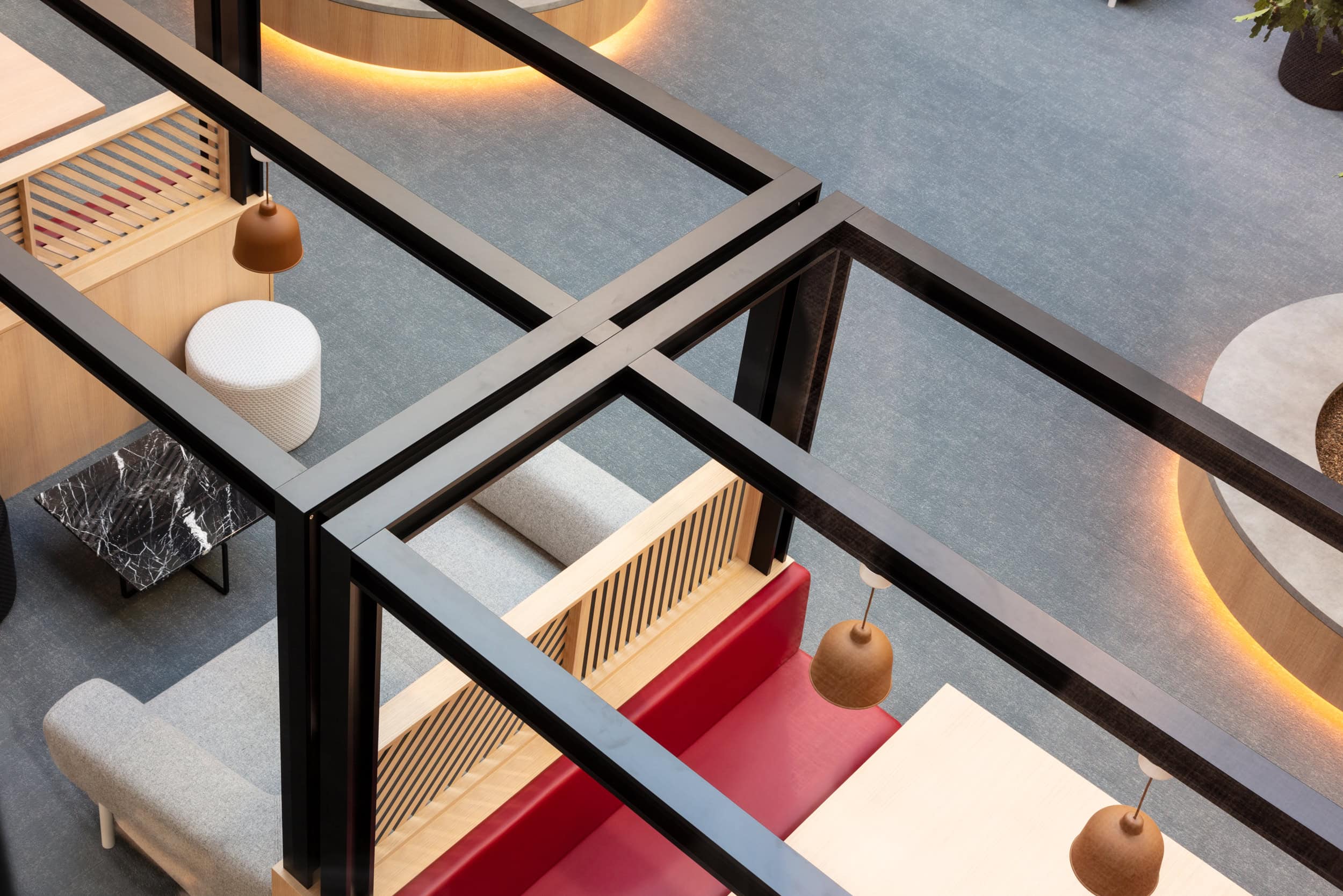 Interior view of a modern seating area featuring a gray sofa, red bench, wooden accents, and pendant lighting, with a marble table and a circular planter in the