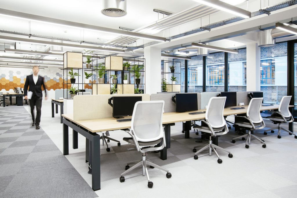 AIS inclusive workplace design and build for Versus Arthritis open plan work zone with banks of desks and a person walking down the hallway