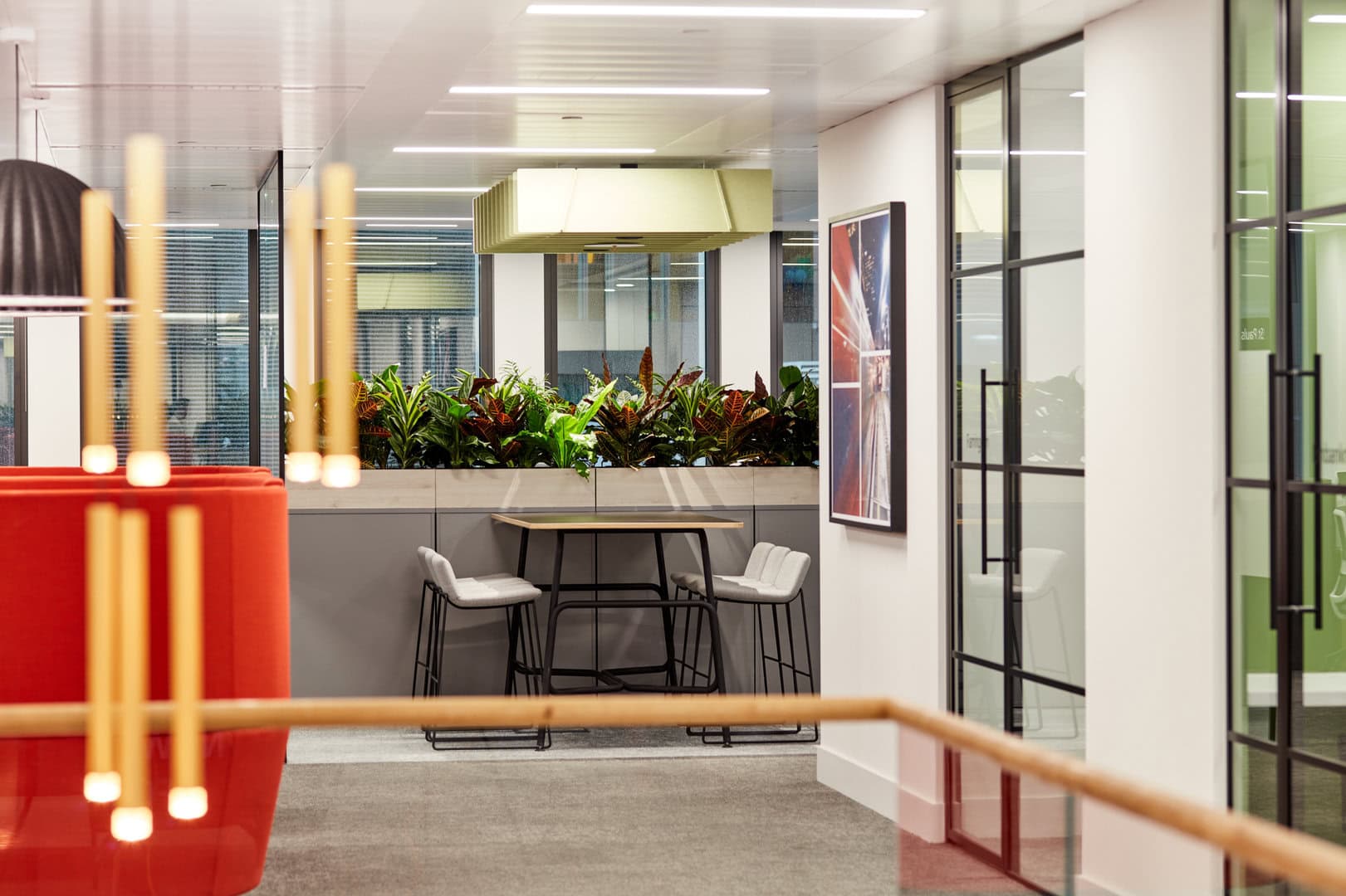 A feature pendant light is shown in the foreground of an image of an office. Some meeting room doors are to the right and a high bench top table is at the back of the room.