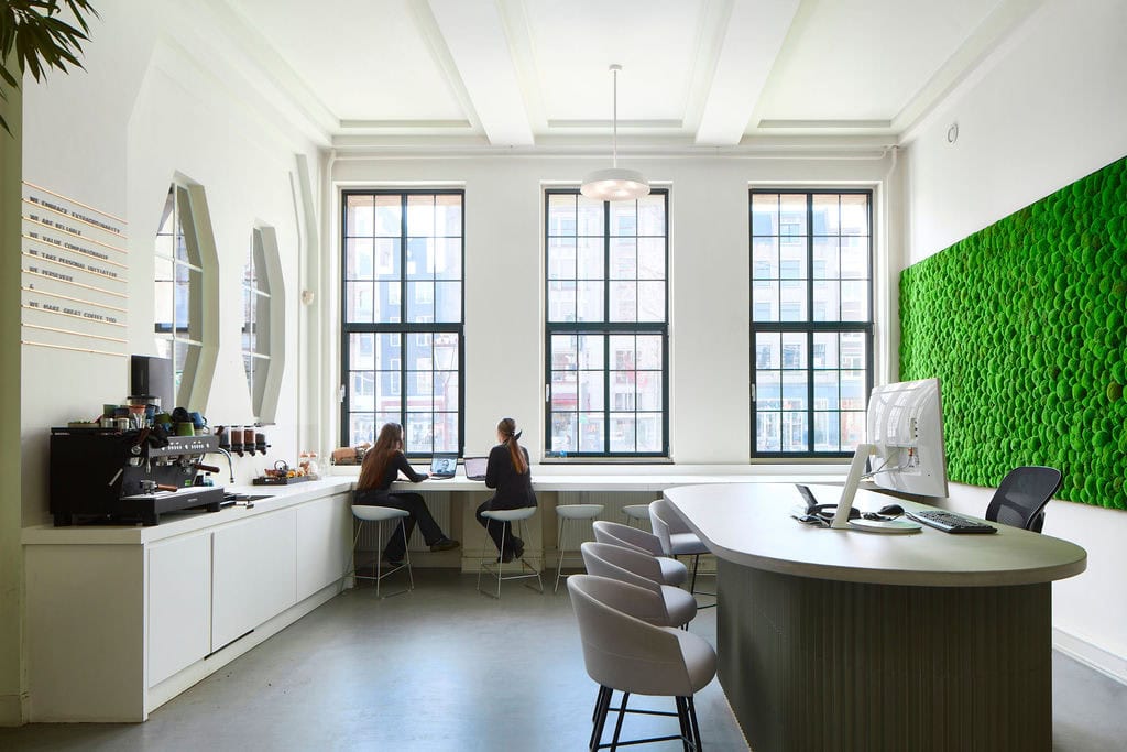 Two colleagues are working at a window bench seat inside the Ohpen Amsterdam office designed and built by AIS.