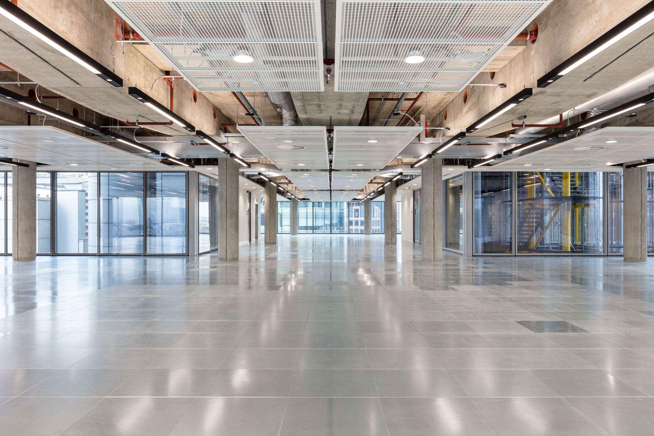 Spacious interior of a modern commercial building featuring polished concrete floors, exposed ceilings, and large glass windows.
