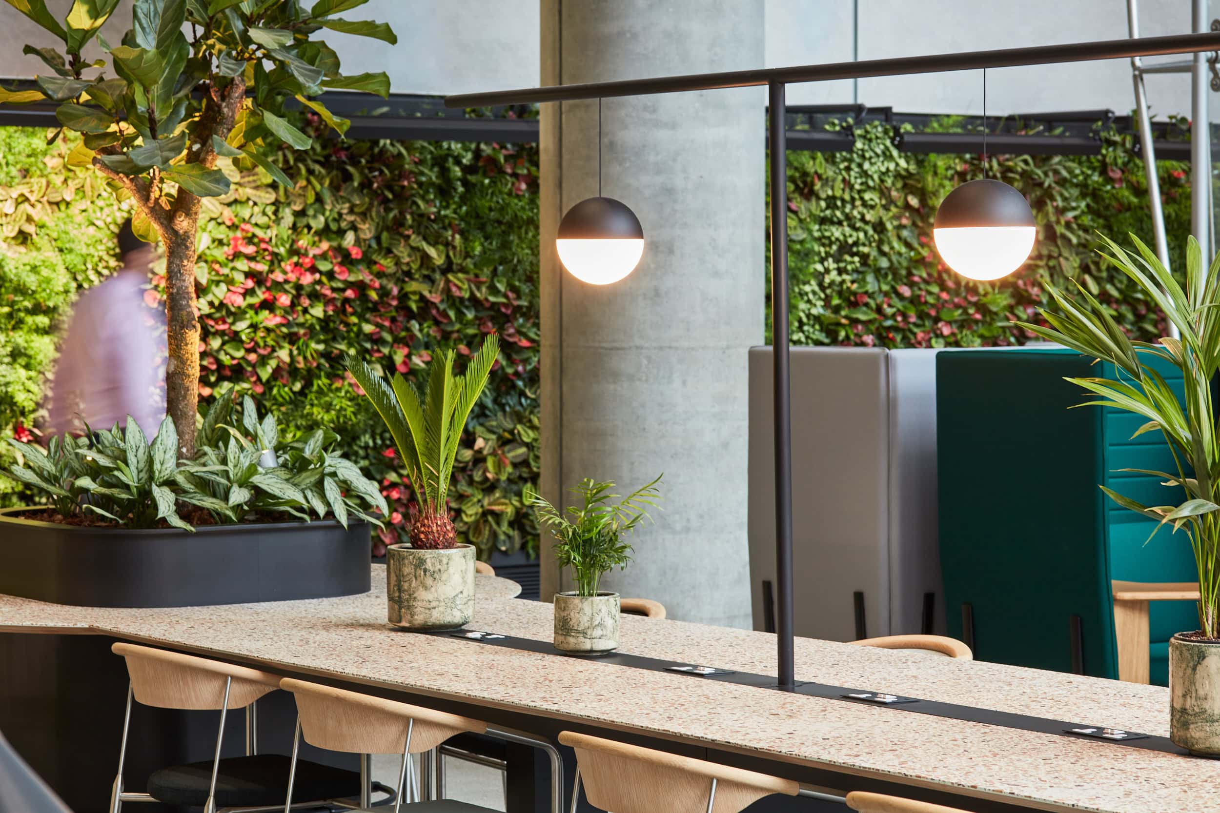 Reception area featuring a green wall with various plants, a long table with wooden chairs, and modern pendant lighting.