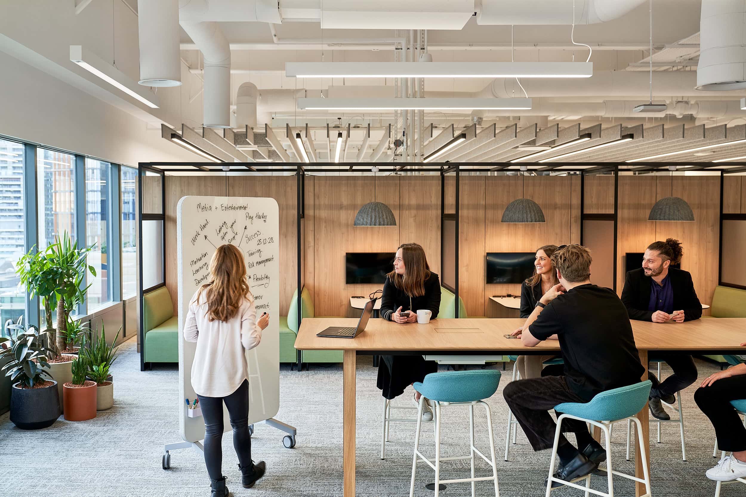 AIS Workplace Strategy meeting, woman presenting on white board to others sat at desk in office