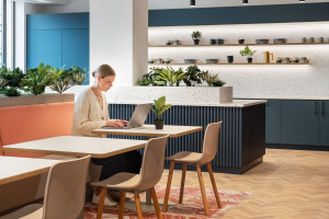 A woman working on a laptop at a modern workspace with plants and a minimalist design.