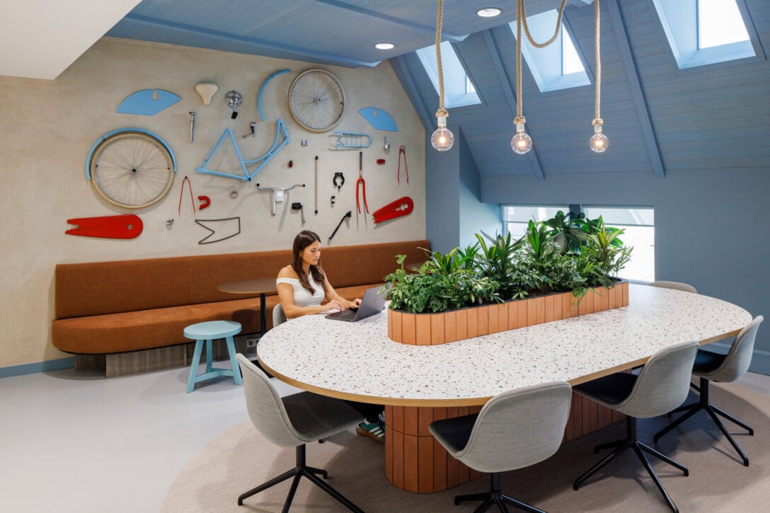 Woman at desk in a collaboration area. The back wall has a deconstructed bicycle attached to it.