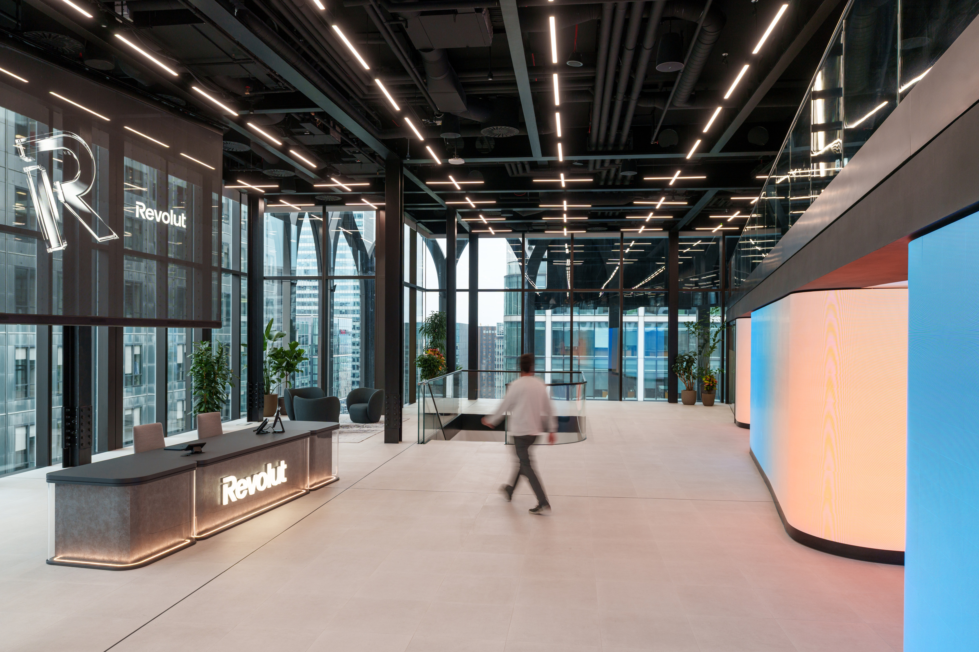 Modern office interior of Revolut in London, featuring a reception desk with the company logo, large windows, and contemporary lighting.