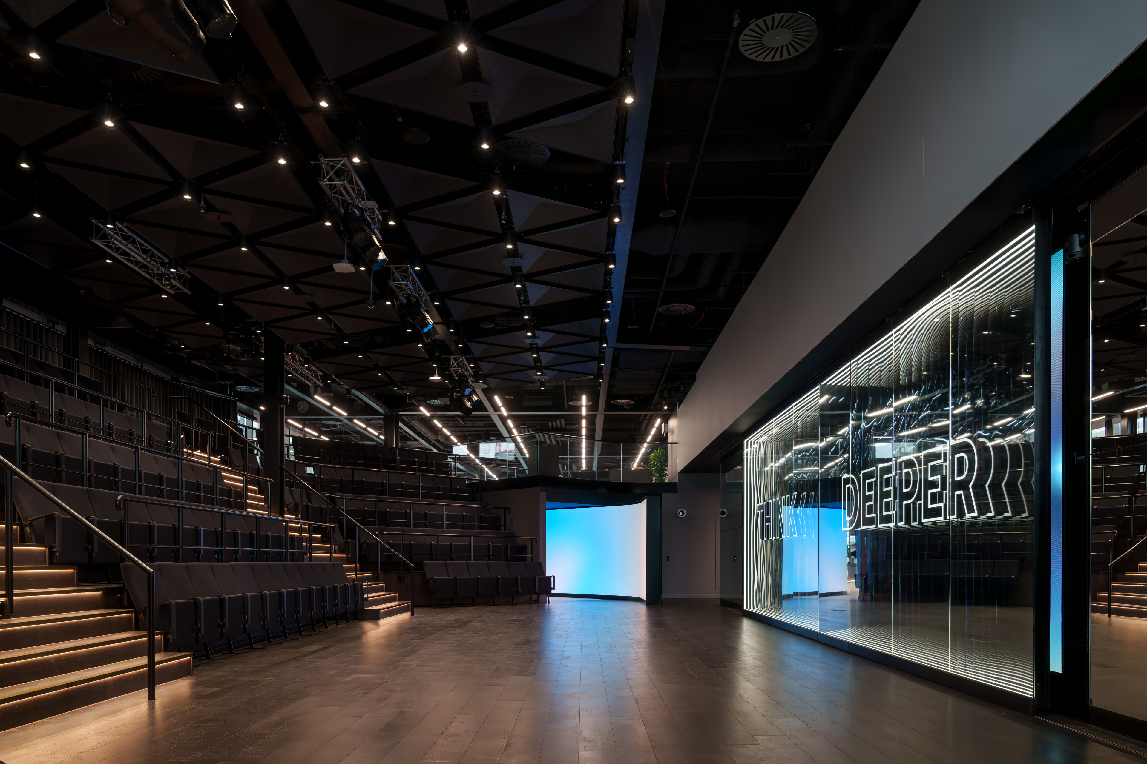 Modern auditorium interior featuring tiered seating, sleek lighting, and a glass wall with the words "THINK DEEPER.