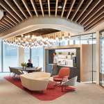Modern office interior featuring a dining area with a large table, stylish seating, and a kitchenette, illuminated by a unique chandelier.