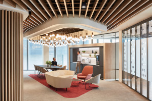 Modern office interior featuring a dining area with a large table, stylish seating, and a kitchenette, illuminated by a unique pendant light fixture.