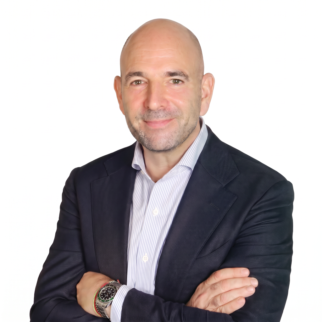 A bald man in a dark blazer and light striped shirt smiles with his arms crossed, wearing a watch on his left wrist.