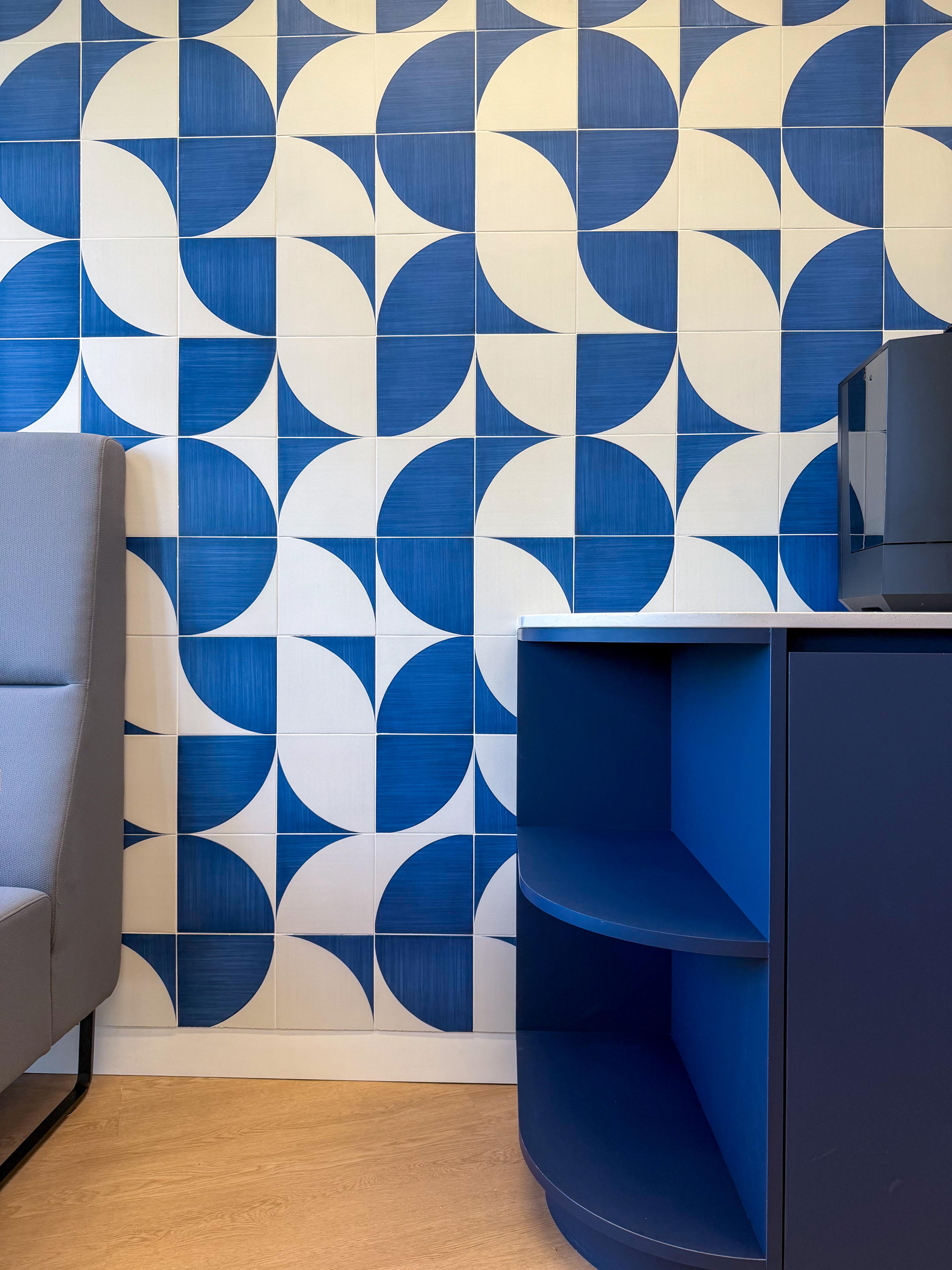 Blue and white geometric patterned wall tiles with a gray chair and a dark blue shelf unit in an office setting.