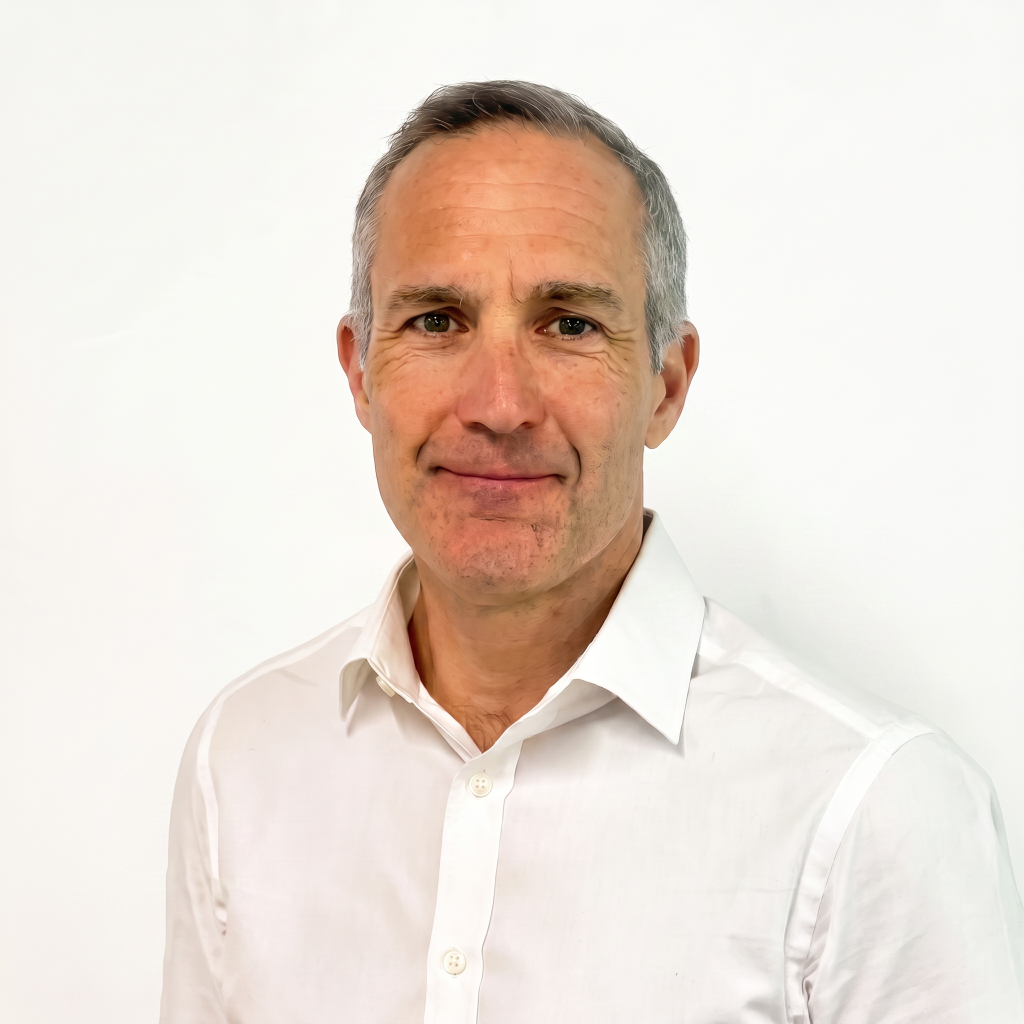 A middle-aged man with short gray hair and a slight smile, wearing a white button-up shirt, stands against a plain white background.