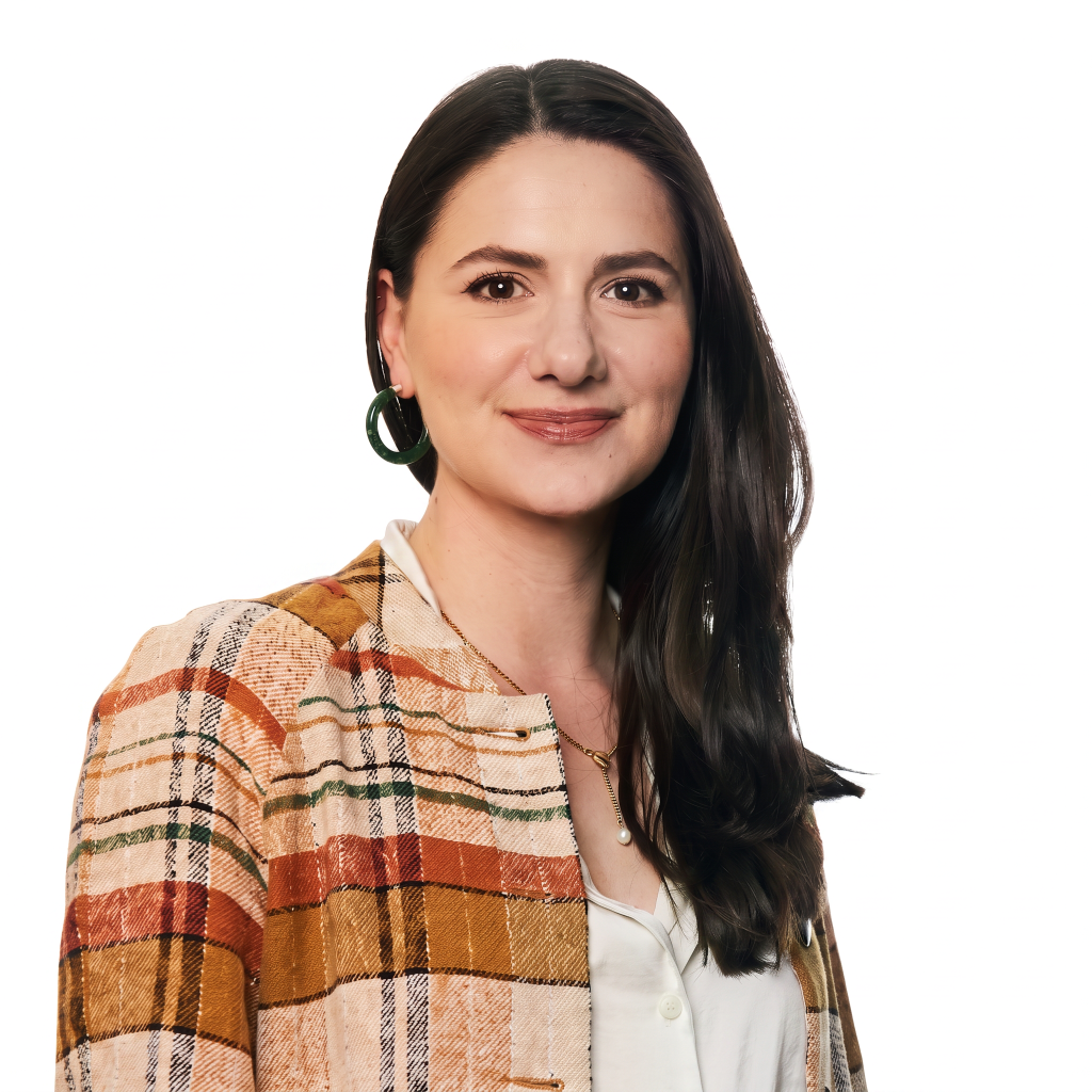 Woman with long dark hair wearing a patterned blazer and green earrings, smiling against a white background.