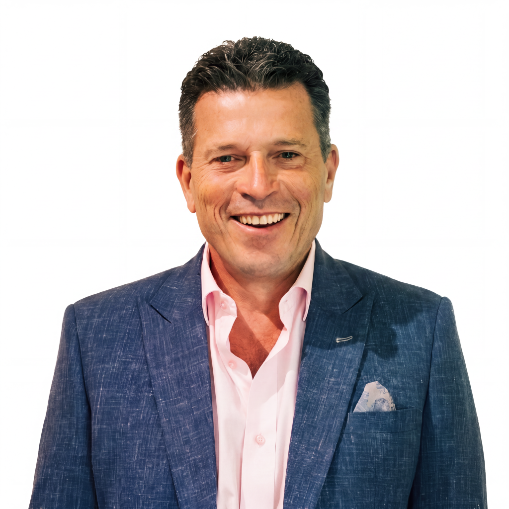 Smiling man wearing a blue blazer over a pink shirt, with a pocket square, against a white background.