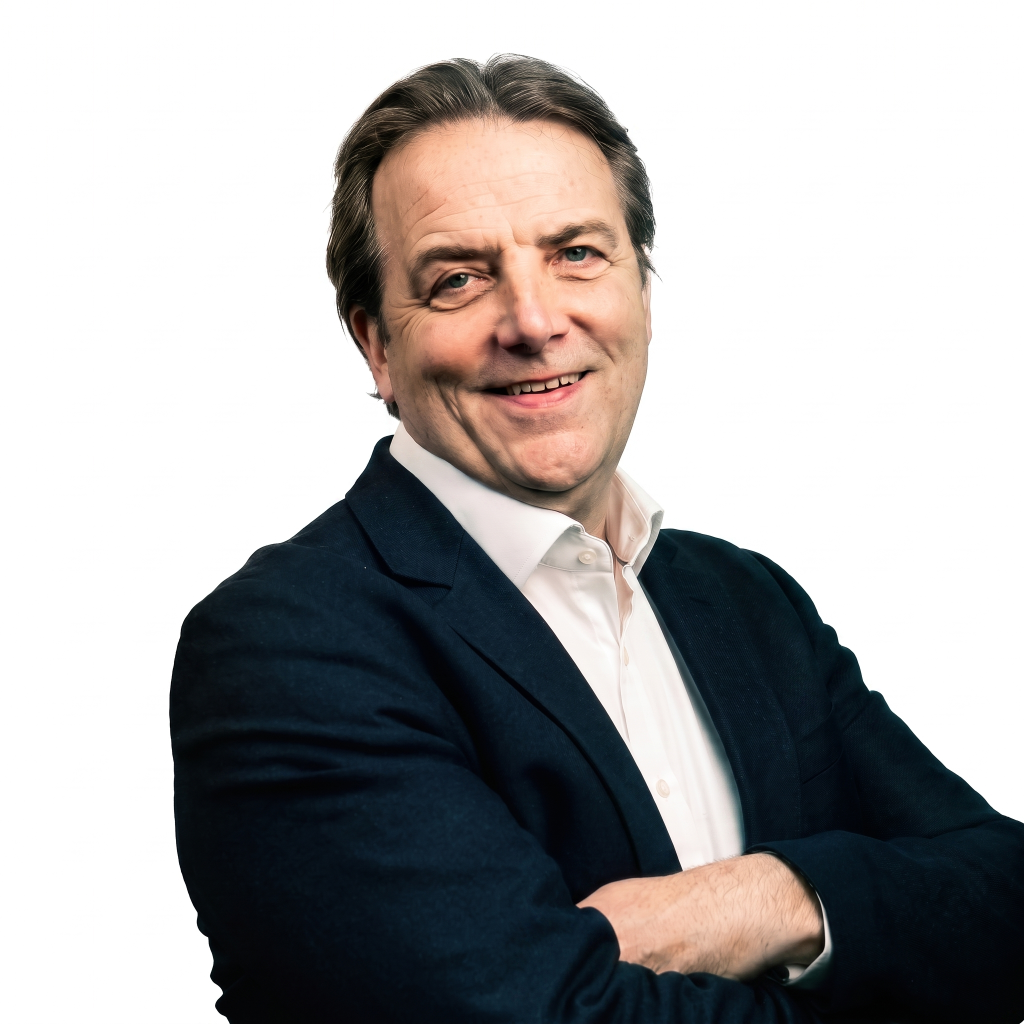 A man with short brown hair and a slight smile, wearing a dark blazer over a white shirt, stands with his arms crossed against a plain white background.