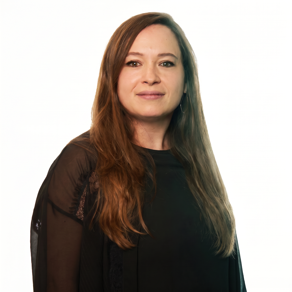 A woman with long brown hair wearing a black top, standing against a white background.