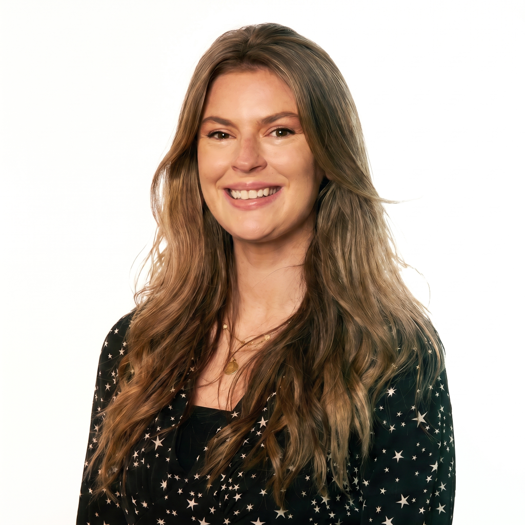 Smiling woman with long, wavy hair wearing a black shirt with white stars against a plain white background.